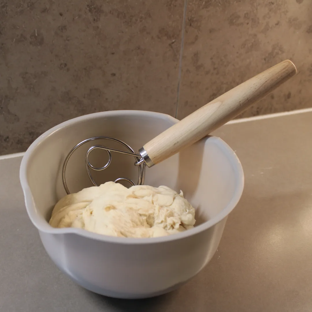 dansk_degvisp_25cm_4 En grå skål med deg och en tradionell dansk degvisp med trähandtag på en grå köksbänk.