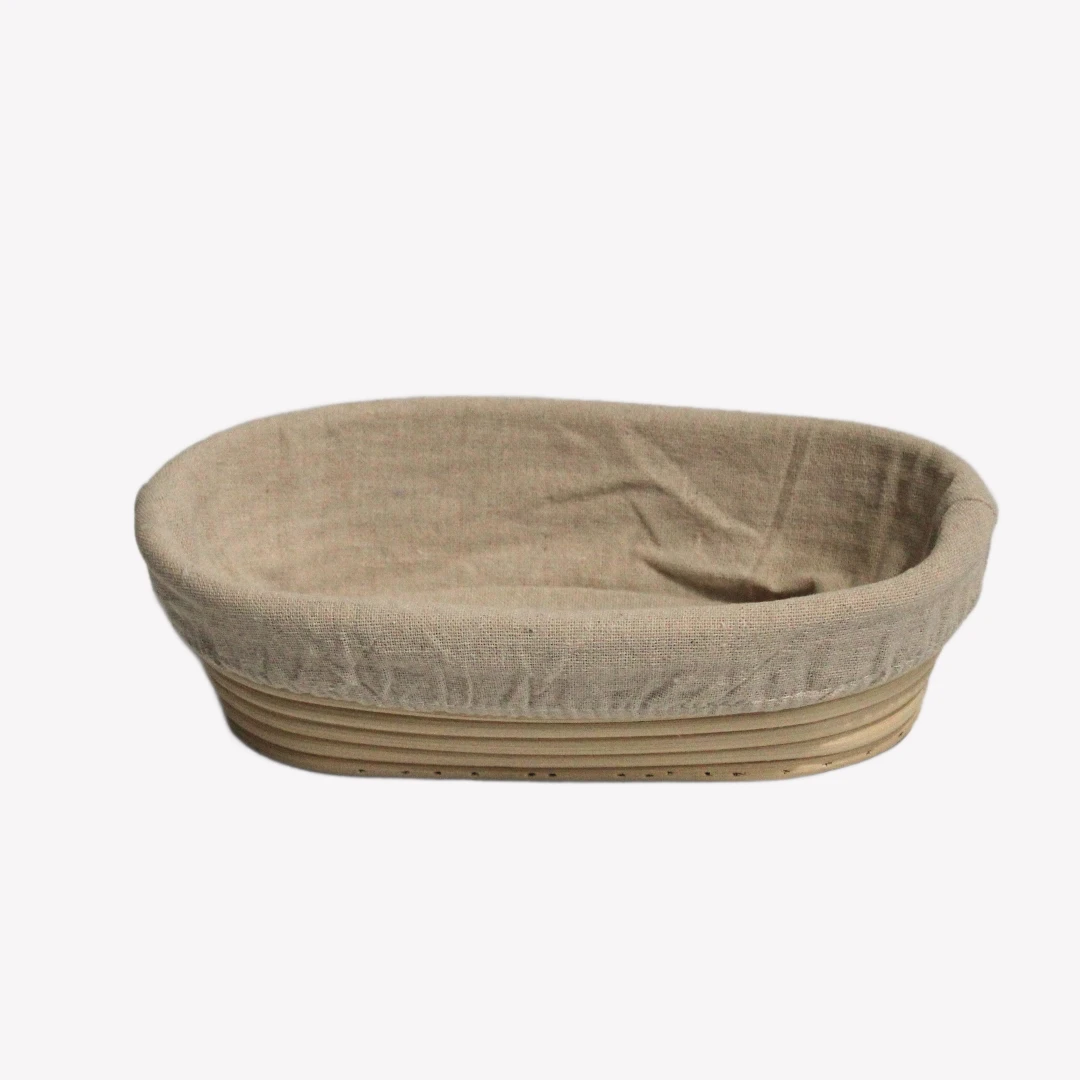 jaskorg_oval_23cm_3_rgba En oval jäskorg 23 cm i rotting med tygöverdrag. Jäskorgen är placerad på en vit bakgrund.