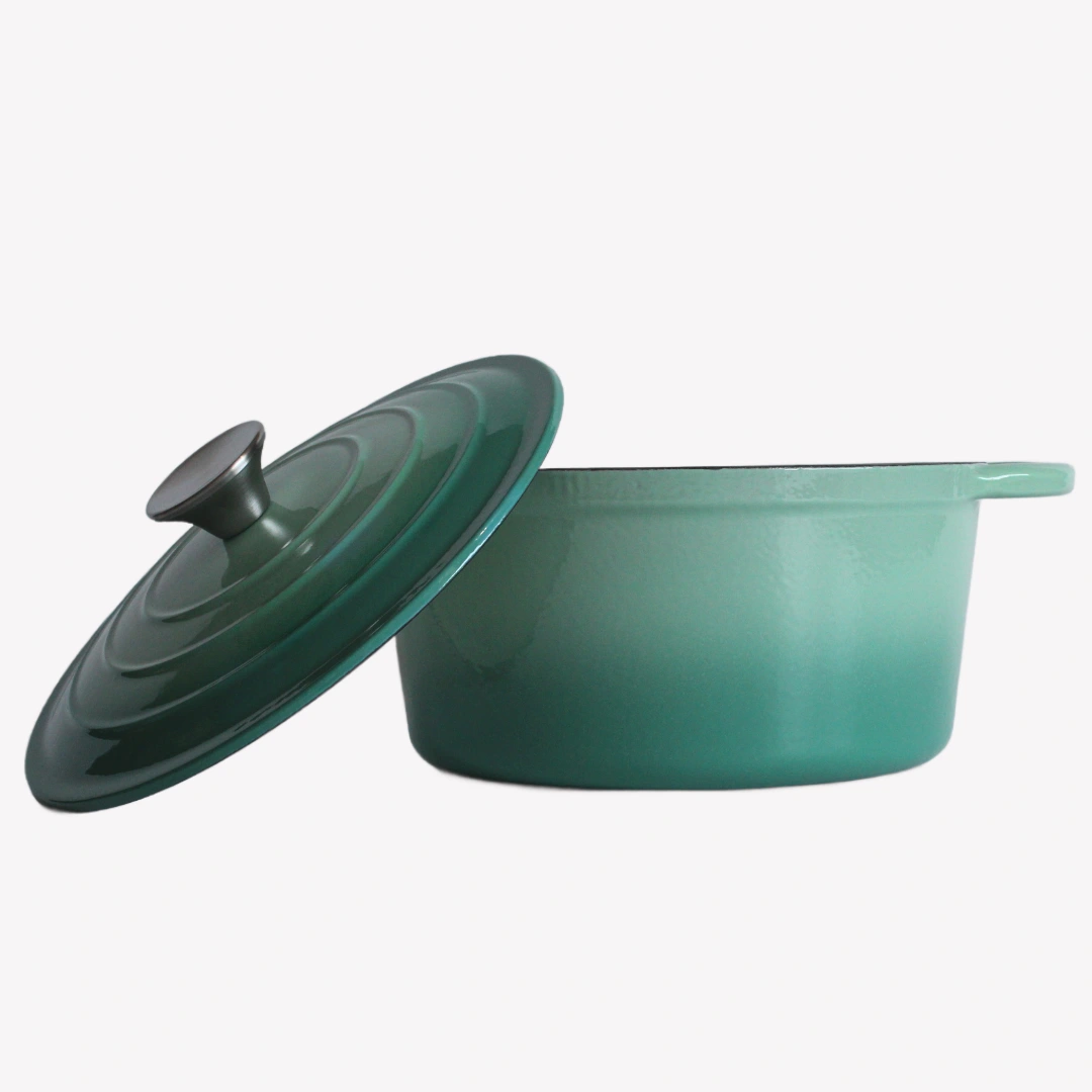 En grön gjutjärnsgryta med locket avtaget. Locket lutar mot grytan, Båda står på en vit bakgrund.