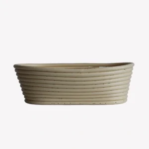 En oval jäskorg i beige plast med en veckad yta. Jäskorgen står på en ljusgrå bakgrund.