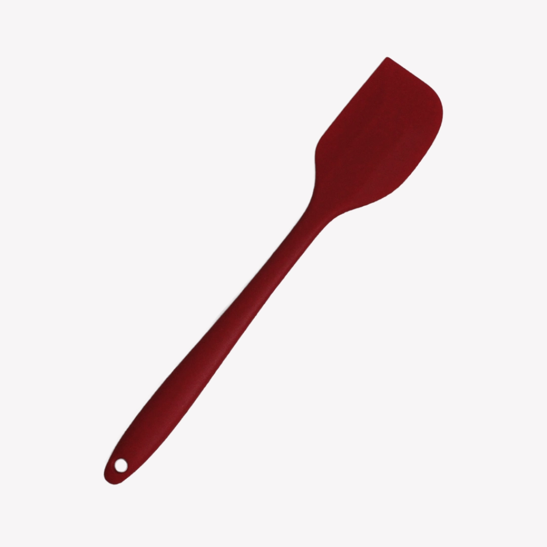 En röd slickepott i silikon med långt handtag och ett hål för upphängning. Slickepotten ligger snett på en vit bakgrund.