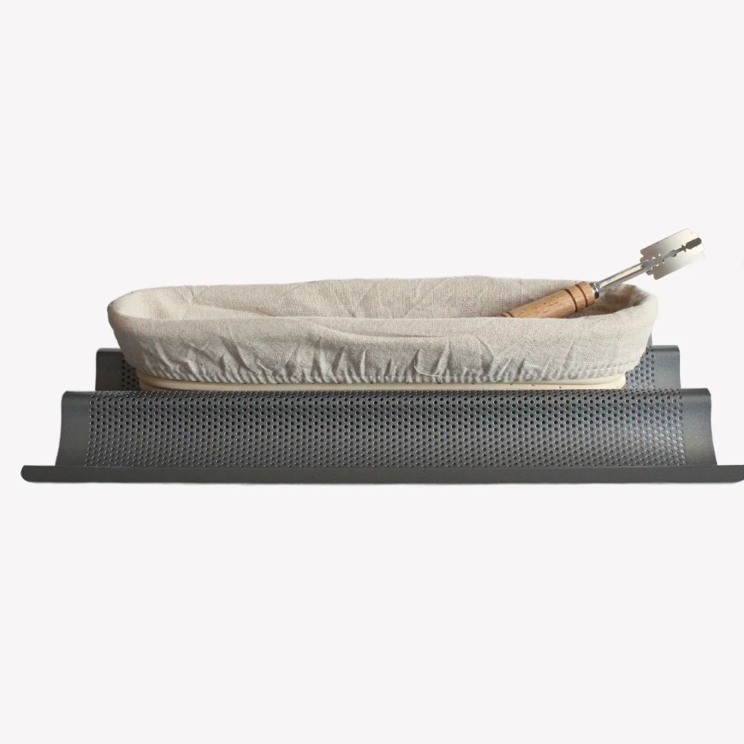 baguettepaket En avlång jäskorg med en snittkniv i trä inuti, stående på en bakplåt i metall.
