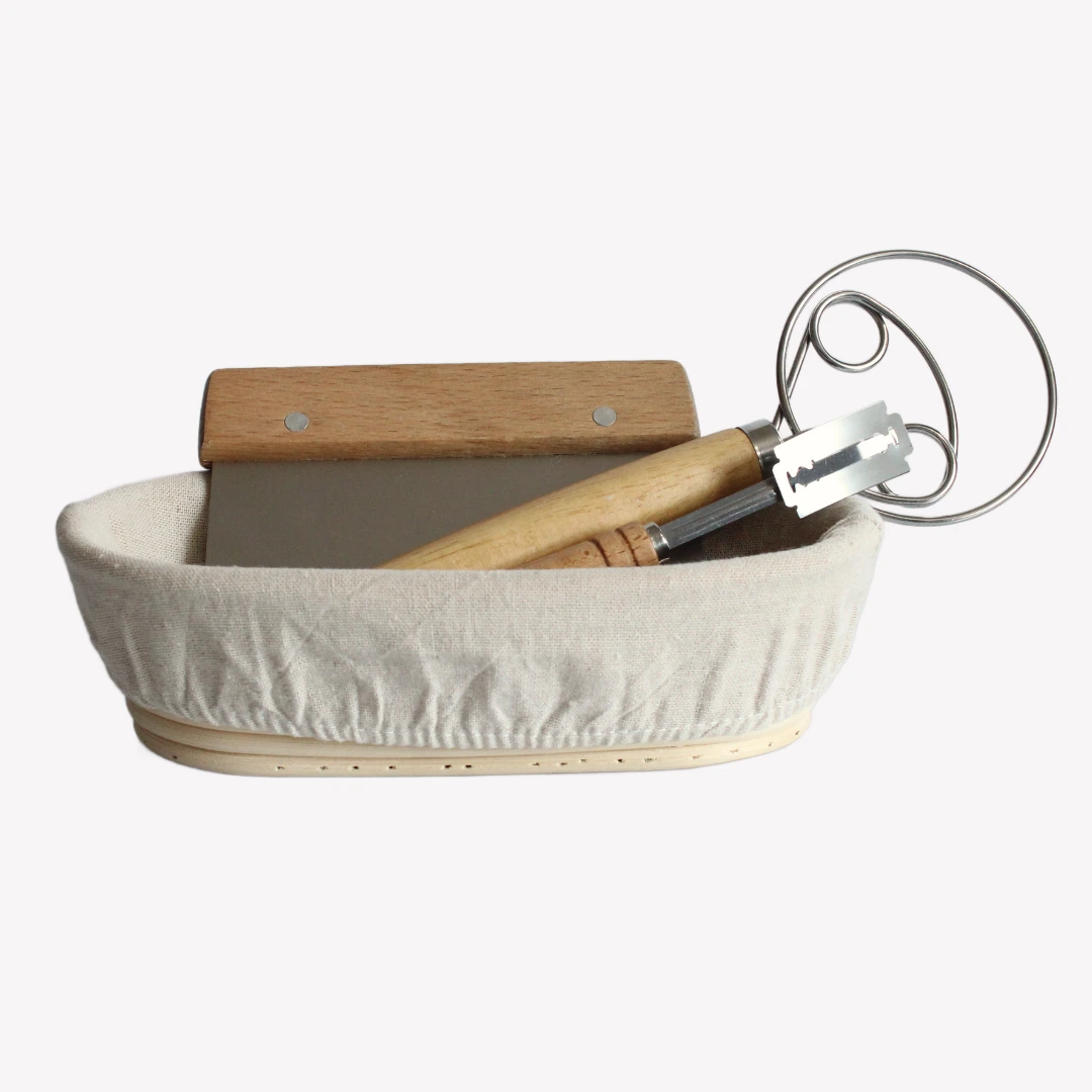En oval jäskorg med en dansk degvisp, en snittkniv i trä och en degskrapa med trähandtag placerade i korgen.