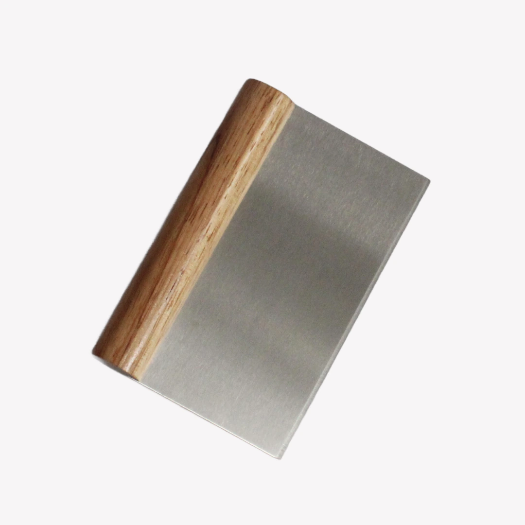 En degskrapa med handtag av ljust trä och ett blad av rostfritt stål ligger på en ljusgrå bakgrund. Handtaget är rundat.