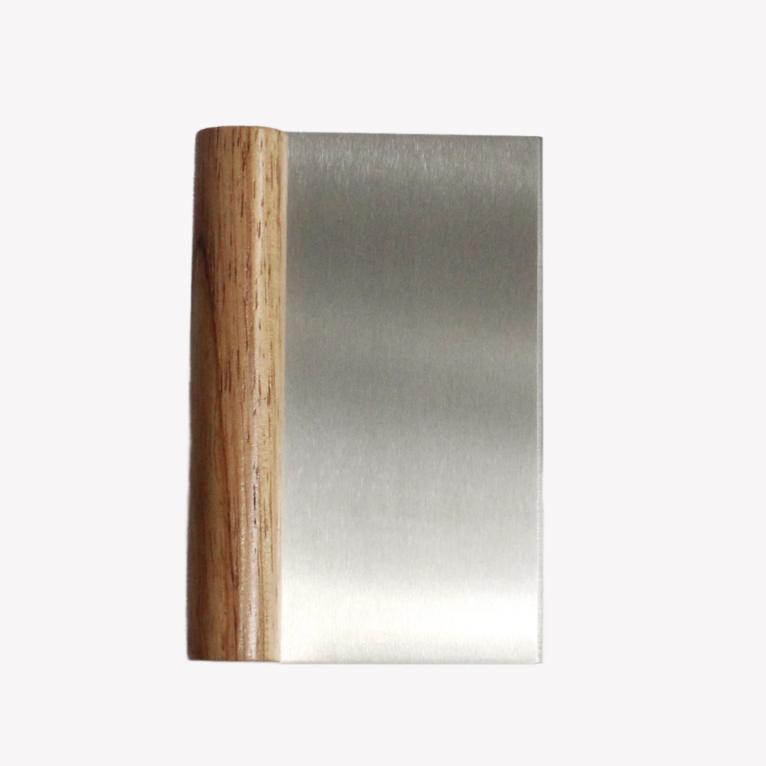 En degskrapa i rostfritt stål med ett runt trähandtag. Degskrapan ligger på en vit bakgrund.