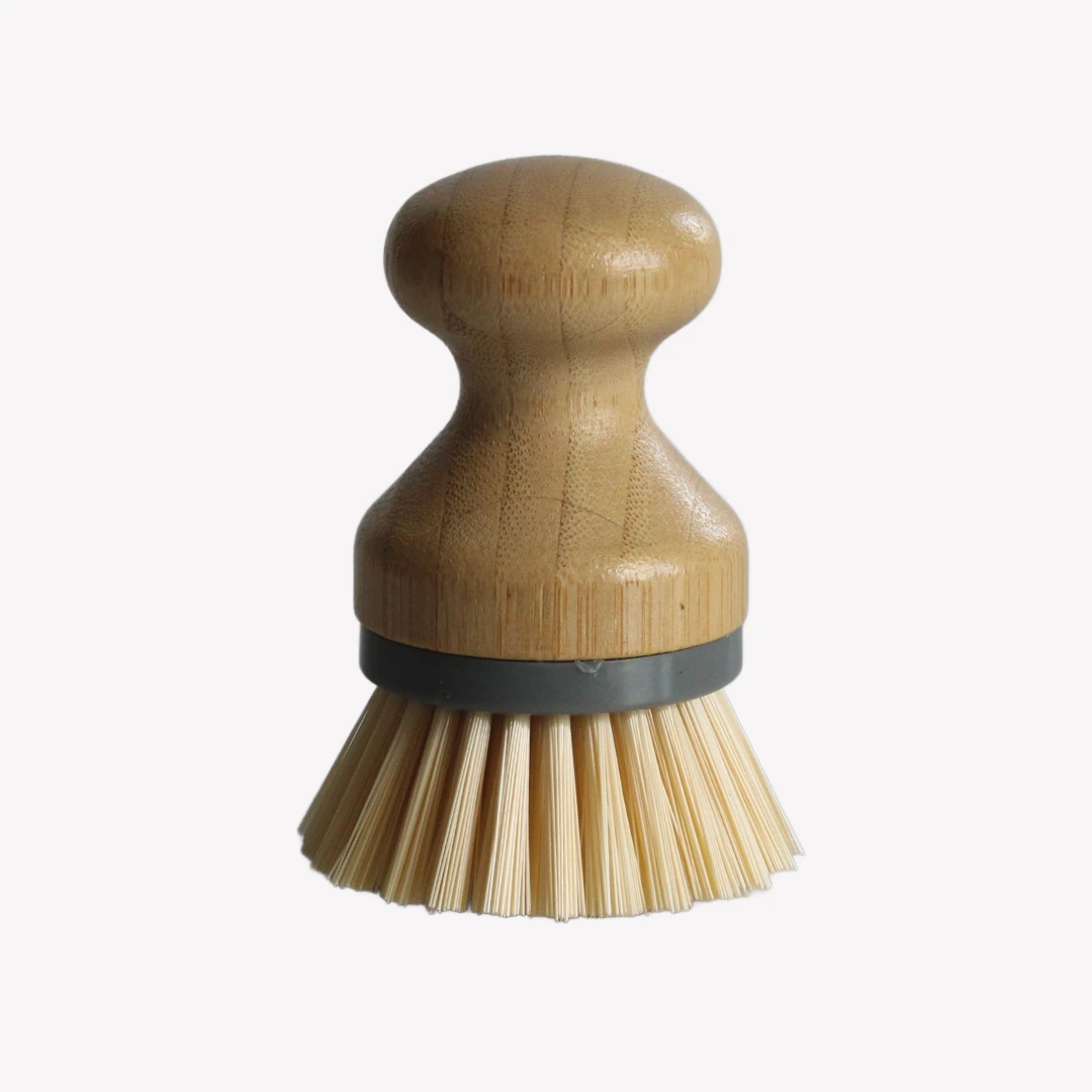 jaskorgsborste_bambu En jäskorgsborste med runt handtag i trä och borstar av bambu står på en vit bakgrund. En grå ring håller ihop handtaget och borsten.