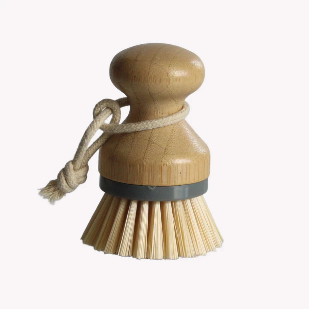 jaskorgsborste_bambu_3 En jäskorgsborste med runt handtag i trä och borstar av bambu står på en vit bakgrund. En grå ring håller ihop handtaget och borsten. Borsten har ett snöre runt handtaget.