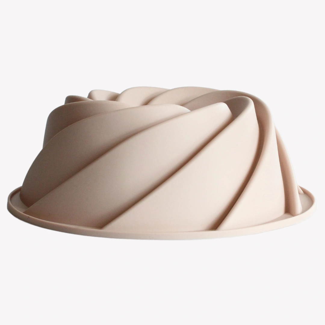 sockerkaksform_silikon_spiral_rosa En rosa sockerkaksform i silikon med spiralformad design, sedd från sidan. Formen har jämna, böljande mönster som skapar en elegant virvelstruktur.