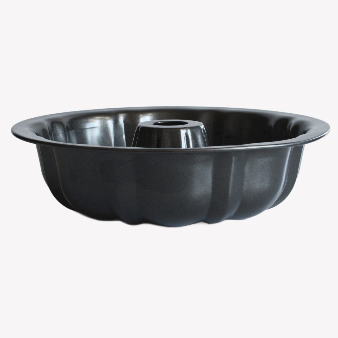 sockerkasform_24cm En svart sockerkaksform i metall med vågig kant och ett hål i mitten. Formen står på en vit bakgrund.