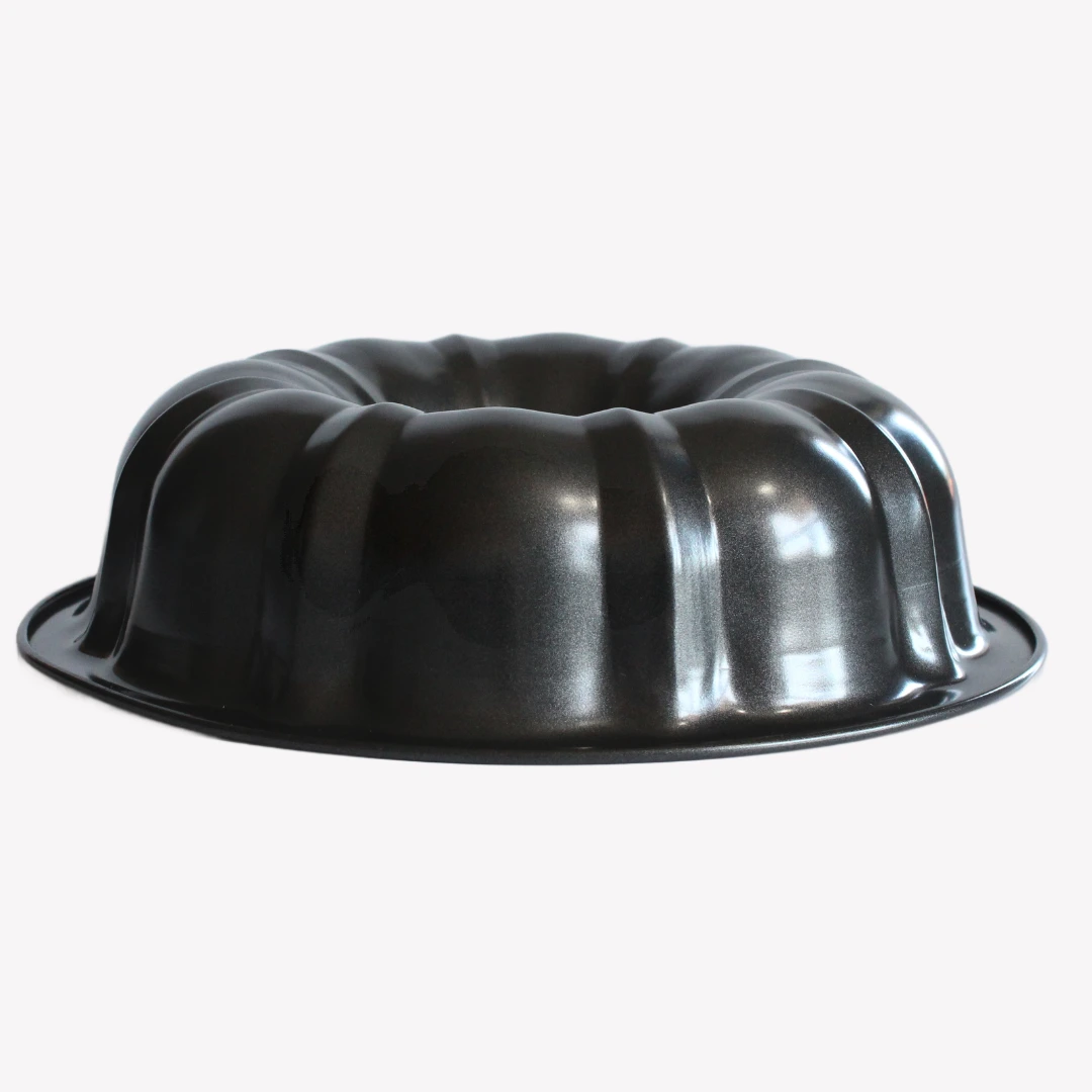 sockerkasform_24cm_2 En svart sockerkaksform i metall med vågig kant och ett hål i mitten. Formen står på en vit bakgrund.