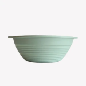 Rund jäskorg i grön silikon med räfflad insida. Jäskorgen ligger på en vit bakgrund