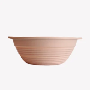 Rund jäskorg i rosa silikon med räfflad insida. Jäskorgen ligger på en vit bakgrund